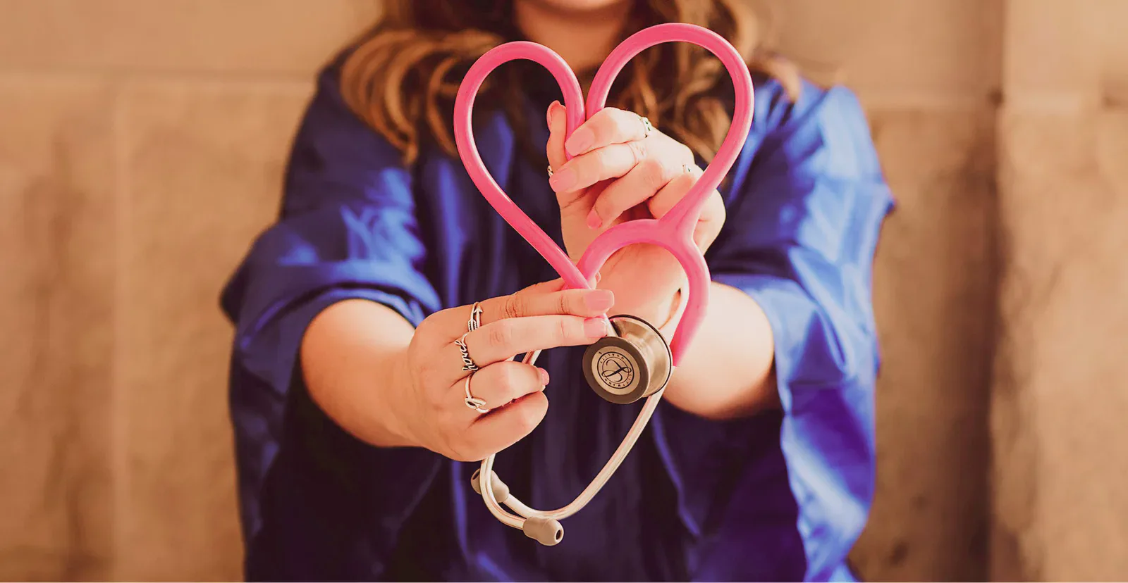 Woman in scrubs holding a stethoscope shaped into a heart