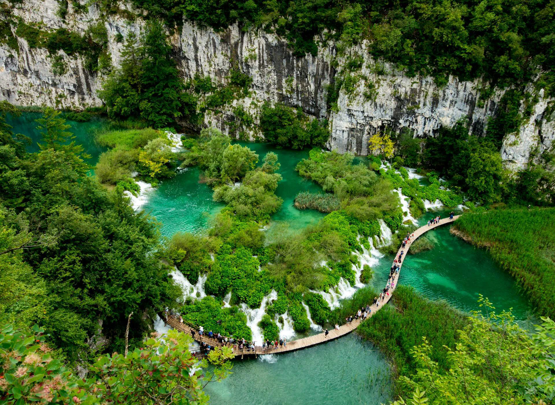 Wooden boardwalk path winding through the turquoise waters and waterfalls of Plitvice Lakes National Park.