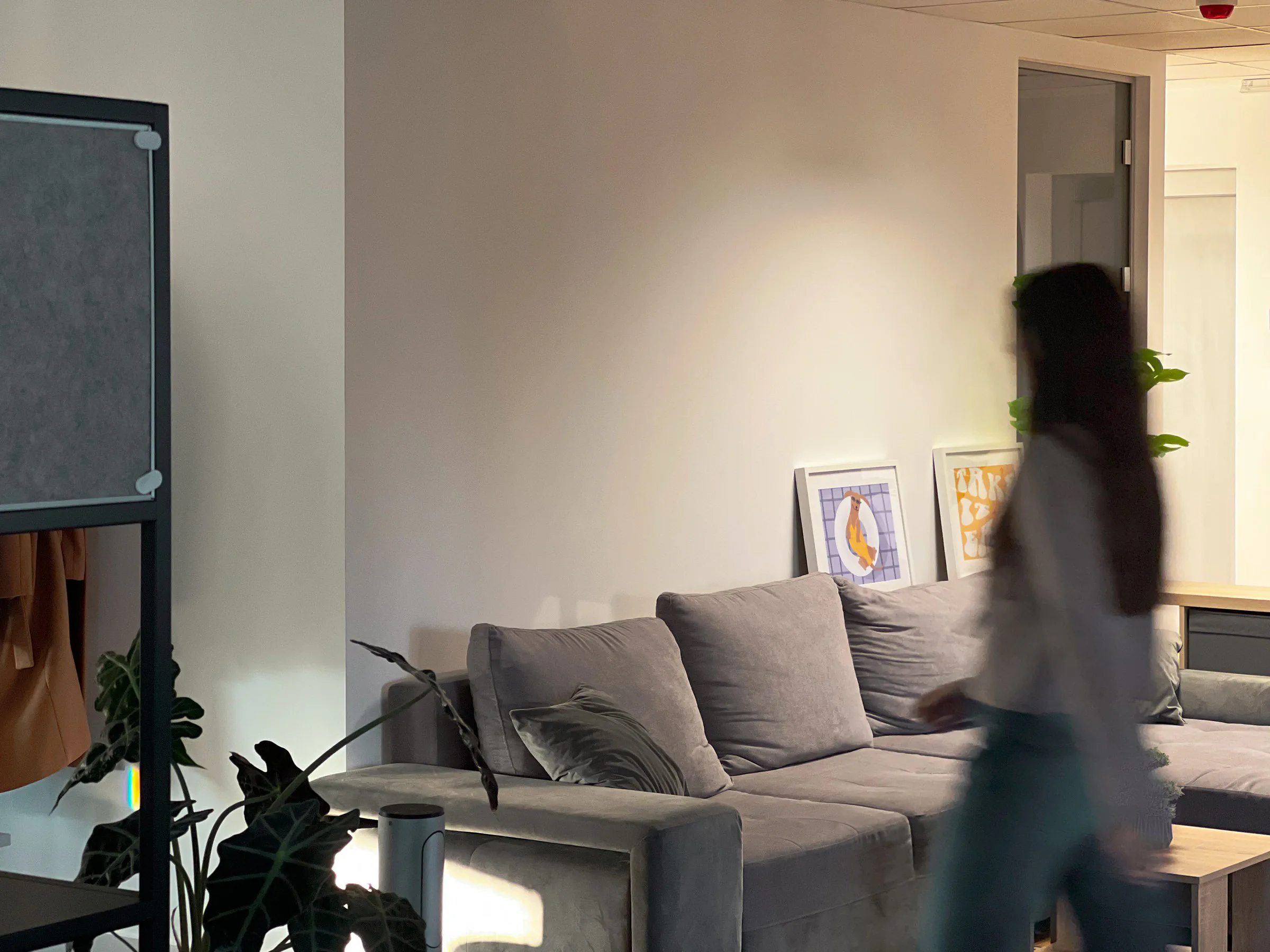 Person walking through an office lounge, motion-blurred, past a couch and framed prints
