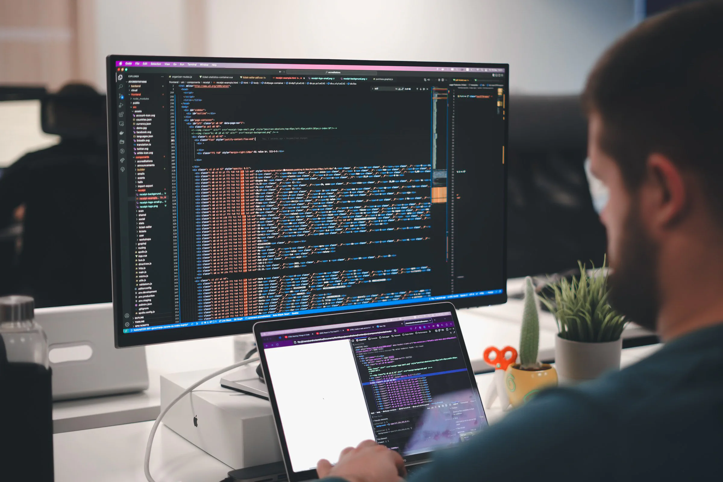 Developer reviewing code across a monitor and laptop at an office desk