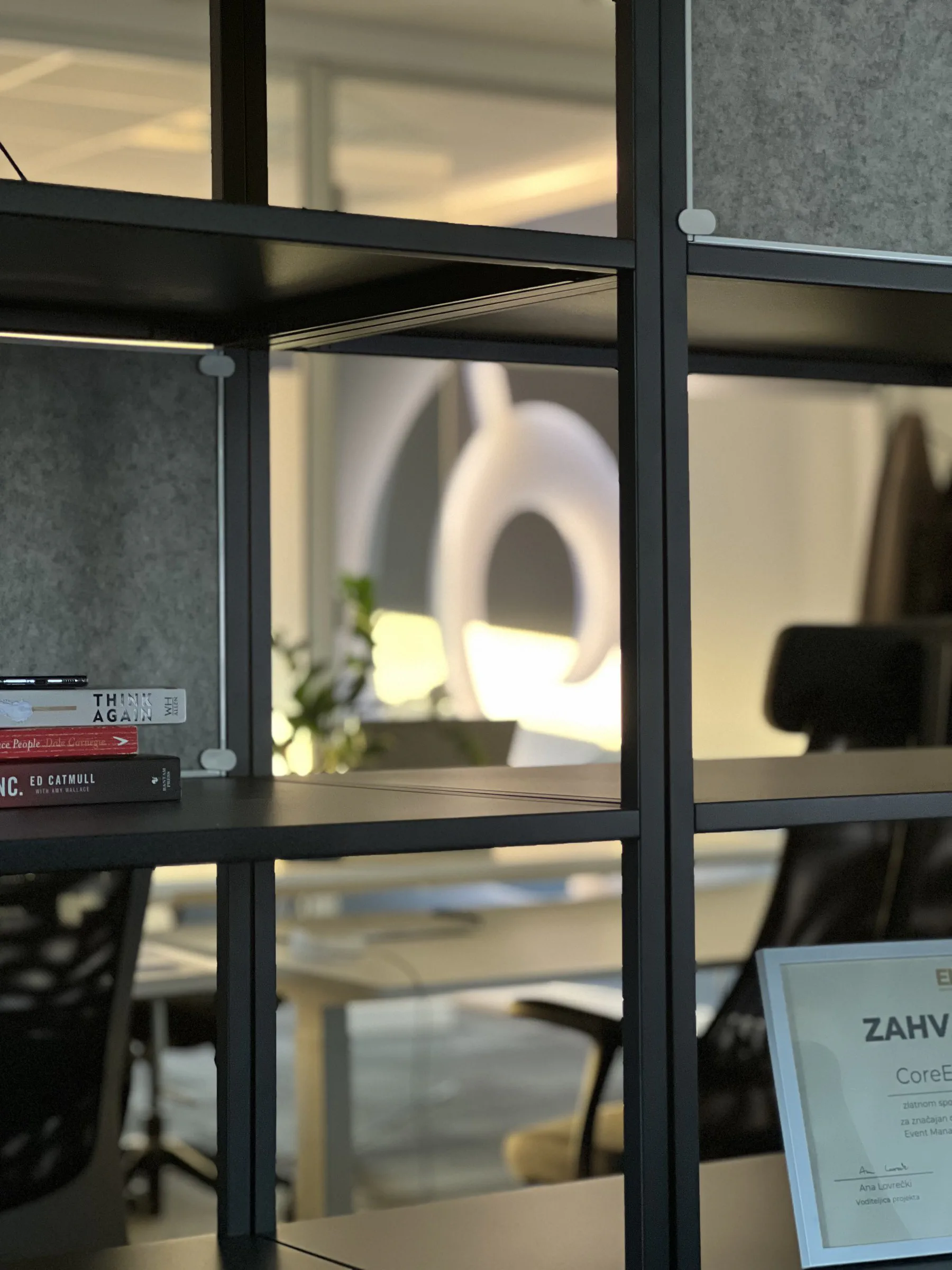 Office shelving with books beside a glass partition, CoreLine's lit-up brand mark visible in the background